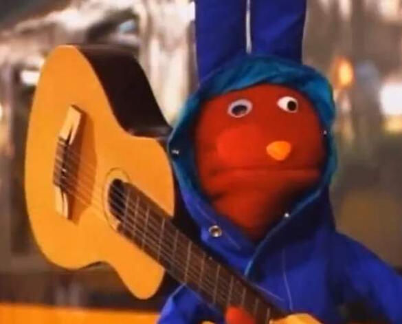 A pic of Bodoque from 31 minutos. He is a red rabbit puppet, he is wearing a raincoat and is holding a guitar over his shoulder
